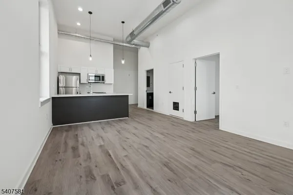 an empty room with wooden floor and kitchen view