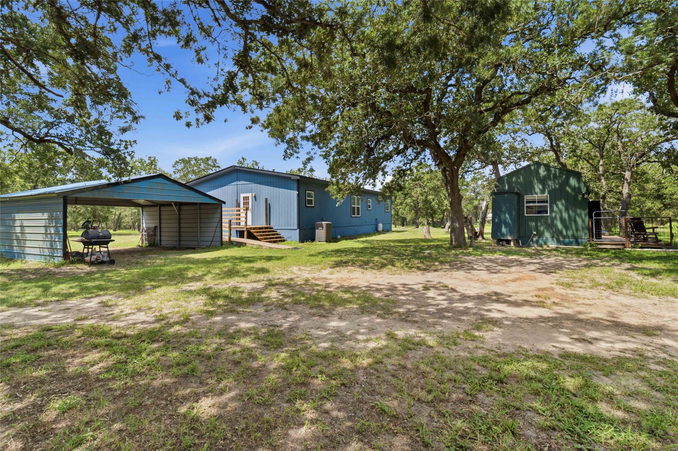 7921 Vista Ranch Road Smithville, TX 78957 - Photo 32 of 39 A spacious lot features a primary residence, a covered carport, and a detached outbuilding amidst mature shade trees.