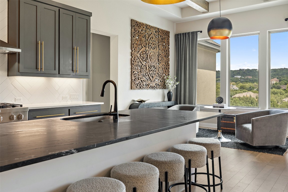 2220 Normandy View Leander, TX 78641 - Photo 19 of 40 Kitchen featuring decorative light fixtures, dark stone counters, dark wood-style floors, a kitchen breakfast bar, and wall chimney range hood