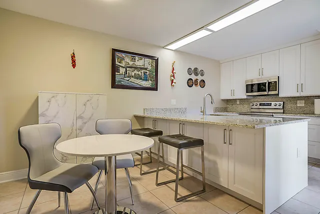 a kitchen with stainless steel appliances kitchen island granite countertop a dining table chairs and a refrigerator