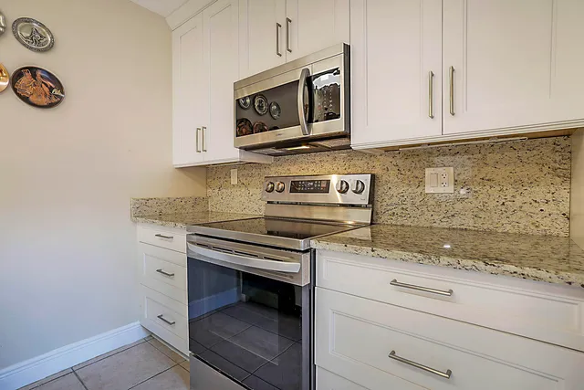 a kitchen with granite countertop white cabinets stainless steel appliances and a counter space