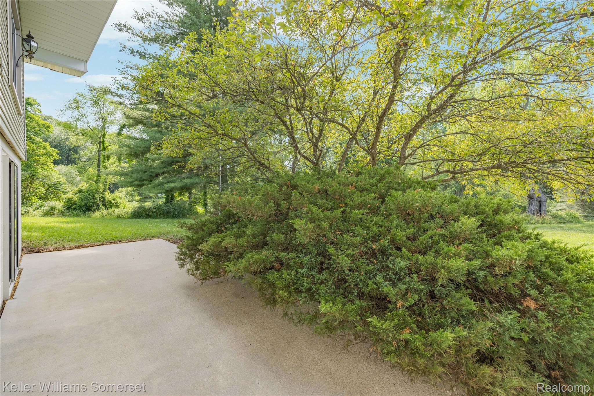 2344 Rochester Road Leonard, MI 48367 - Photo 51 of 66 Expansive concrete patio area with a landscaped border, mature trees, and a spacious grassy area