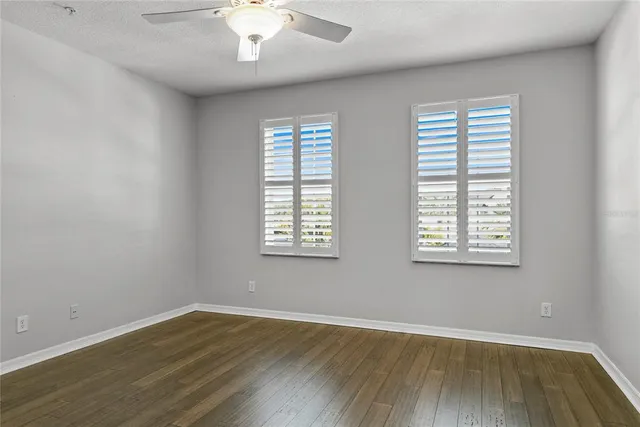 an empty room with wooden floor chandelier fan and windows