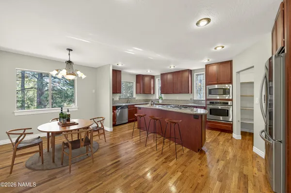 a kitchen with stainless steel appliances granite countertop wooden cabinets a refrigerator a sink a stove a microwave and wooden floors