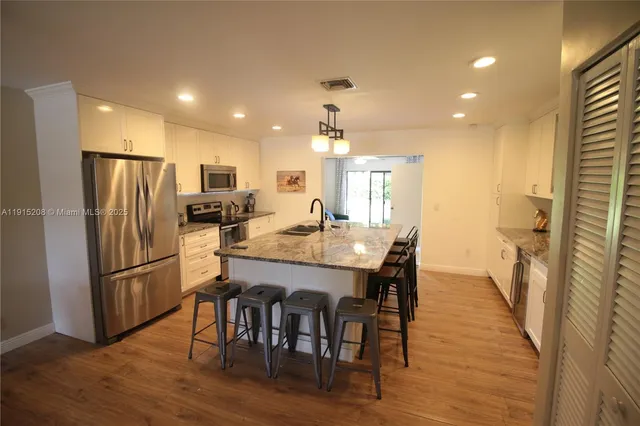 a kitchen with stainless steel appliances granite countertop a refrigerator a stove a sink dishwasher and a dining table with wooden floor