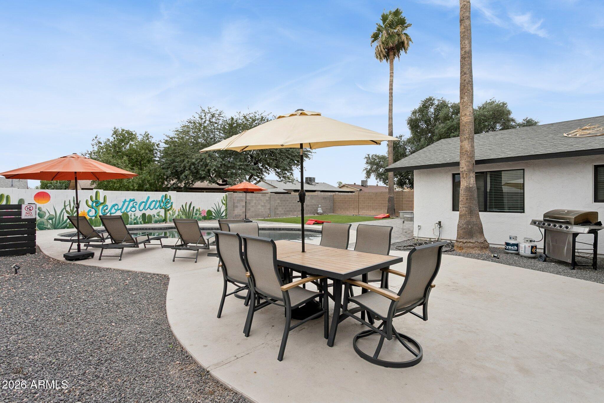 8725 East Osborn Road Scottsdale, AZ 85251 - Photo 26 of 33 a view of a patio with furniture and table under an umbrella with a fire pit and barbeque grill