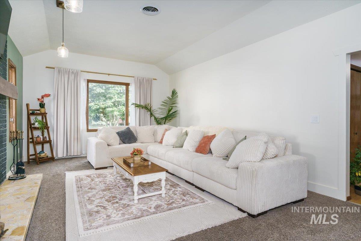 1401 Chokecherry Drive Pocatello, ID 83204 - Photo 6 of 46 Spacious living area featuring a vaulted ceiling, a large window with natural wood trim, and a fireplace with a stone hearth and dark tile surround