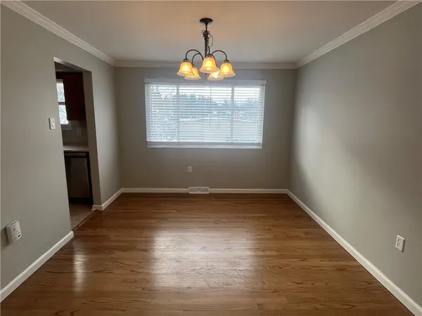 an empty room with wooden floor chandelier and windows