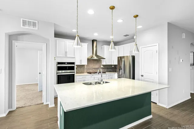 a kitchen with stainless steel appliances kitchen island granite countertop a refrigerator a sink a stove and white cabinets with wooden floor