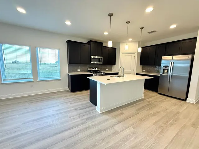 a large kitchen with stainless steel appliances a large counter top a stove a refrigerator and a sink