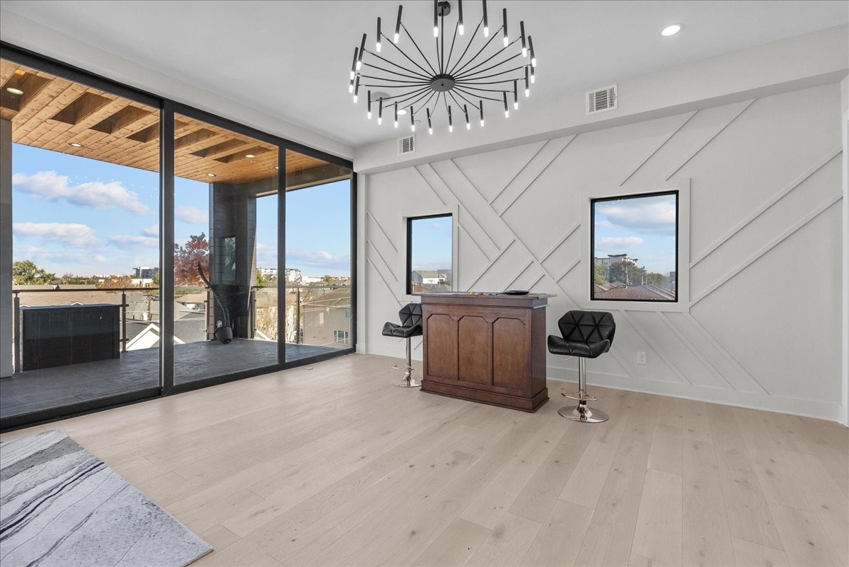 516 Reinerman Street Houston, TX 77007 - Photo 41 of 42 This modern space features large glass doors leading to a spacious balcony with great views. Inside, there's a stylish chandelier, light wood flooring, a chic accent wall, and a small bar area with stools, perfect for entertaining.