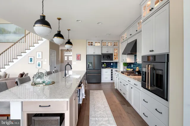 a kitchen with stainless steel appliances kitchen island granite countertop a refrigerator a stove a sink a dining table and chairs with wooden floor