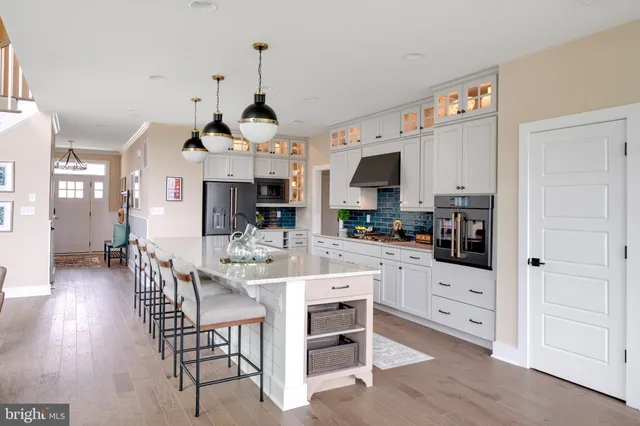 a kitchen with stainless steel appliances kitchen island granite countertop a refrigerator a stove a dining table and chairs with wooden floor