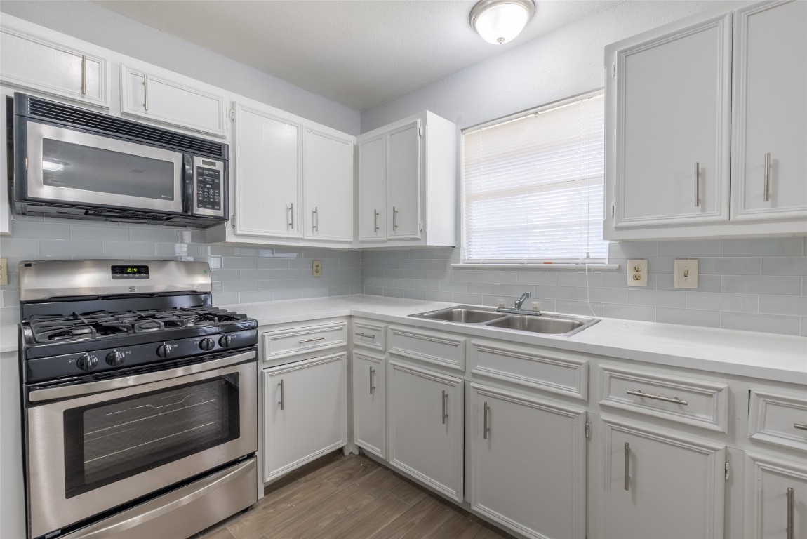Kitchen with stainless steel appliances, white cabinets, light countertops, tasteful backsplash, and light wood-type flooring
