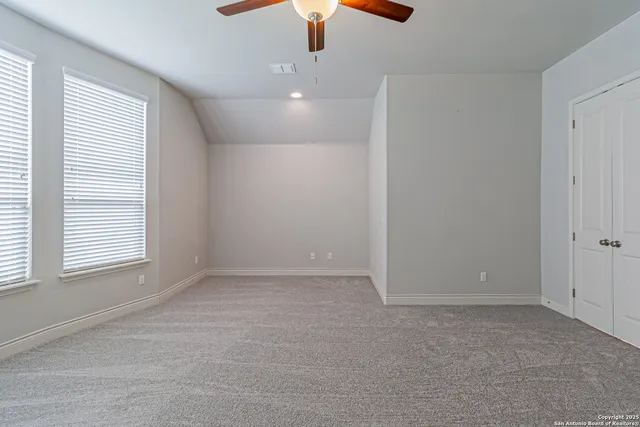 an empty room with chandelier fan and windows