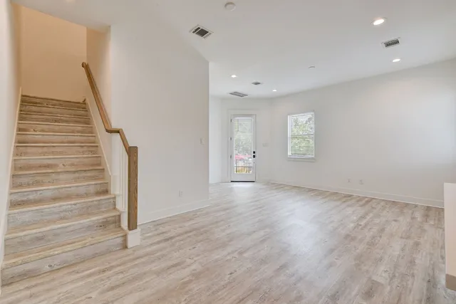 a view of an empty room with wooden floor and stairs