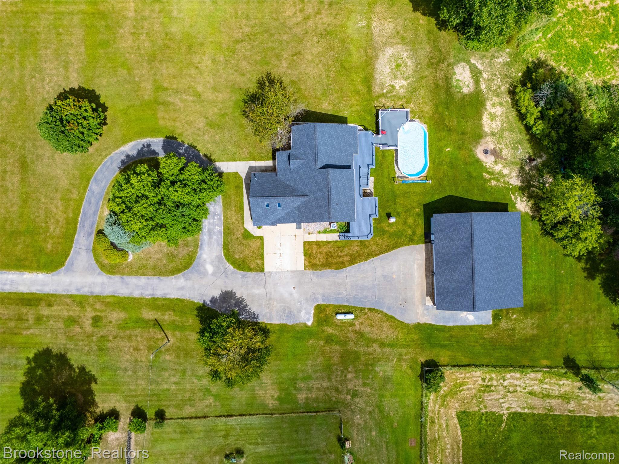 1775 Dutcher Road Howell, MI 48843 - Photo 41 of 41 Expansive green grounds featuring a main residence with a dark shingled roof, a separate detached structure, a paved driveway, and an oval pool with surrounding decking