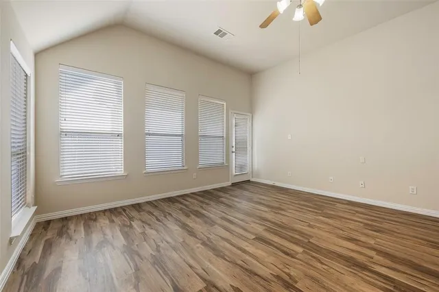 an empty room with wooden floor chandelier fan and windows