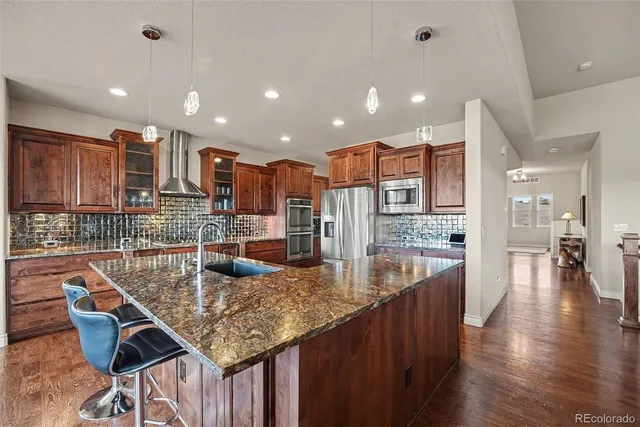 a kitchen with stainless steel appliances kitchen island granite countertop a table chairs in it and wooden floors