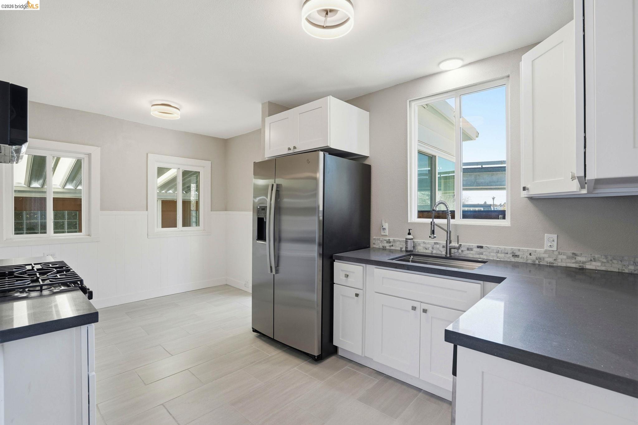840 Key Rte Boulevard Albany, CA 94706 - Photo 12 of 43 Kitchen featuring wainscoting, stainless steel refrigerator with ice dispenser, white cabinets, and dark stone counters