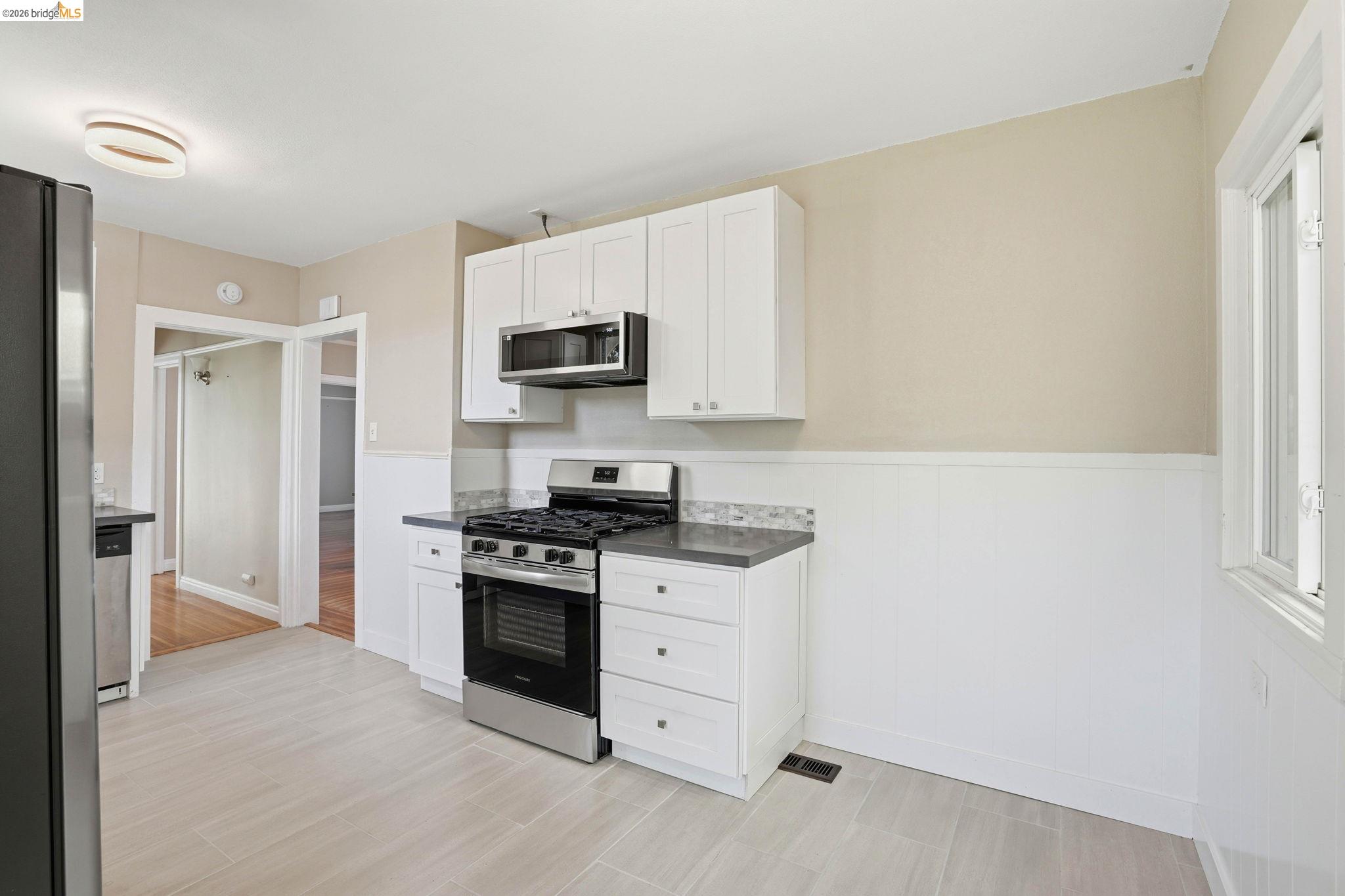 840 Key Rte Boulevard Albany, CA 94706 - Photo 13 of 43 Kitchen featuring stainless steel appliances, white cabinets, a wainscoted wall, and dark countertops