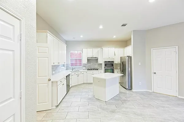 a kitchen with stainless steel appliances granite countertop a stove top oven a refrigerator a sink and white cabinets