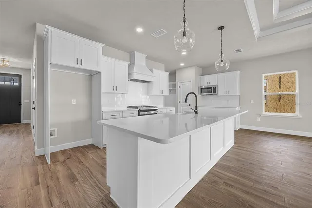 a large kitchen with kitchen island a sink dishwasher a refrigerator and white cabinets with wooden floor