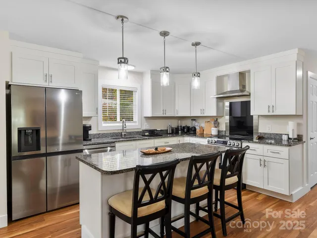 a kitchen with stainless steel appliances granite countertop a sink a stove a refrigerator cabinets a dining table and chairs