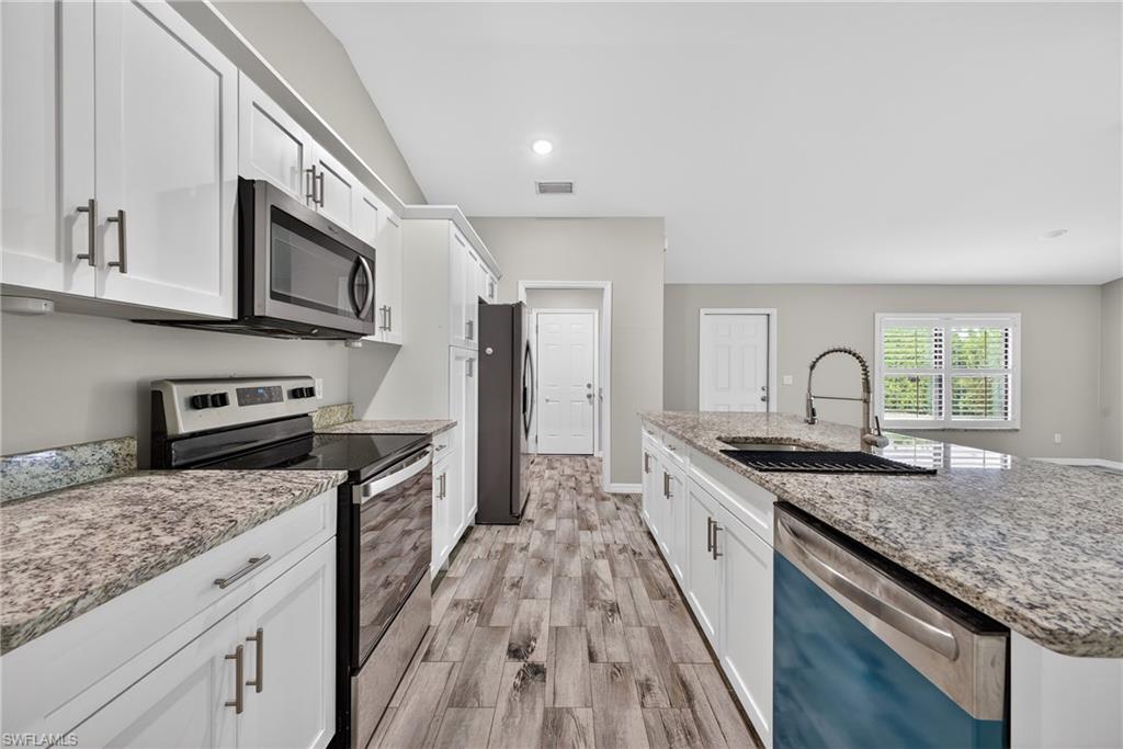 8422 Cardinal Road Fort Myers, FL 33967 - Photo 7 of 24 Kitchen featuring stainless steel appliances, white cabinetry, light stone counters, a center island with sink, and recessed lighting