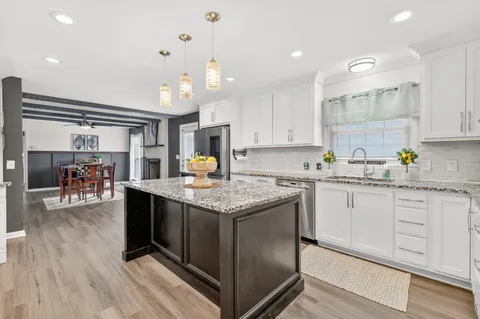 a kitchen with granite countertop a stove top oven a sink dishwasher and white cabinets with wooden floor
