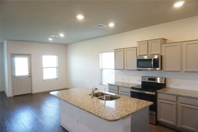 a kitchen with granite countertop kitchen island stainless steel appliances a sink stove and cabinets