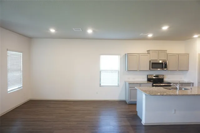 a kitchen with stainless steel appliances granite countertop a stove a sink a refrigerator white cabinets and wooden floor