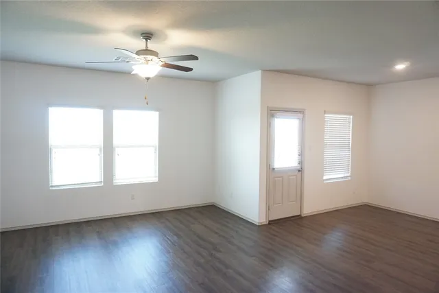 an empty room with wooden floor chandelier fan and windows