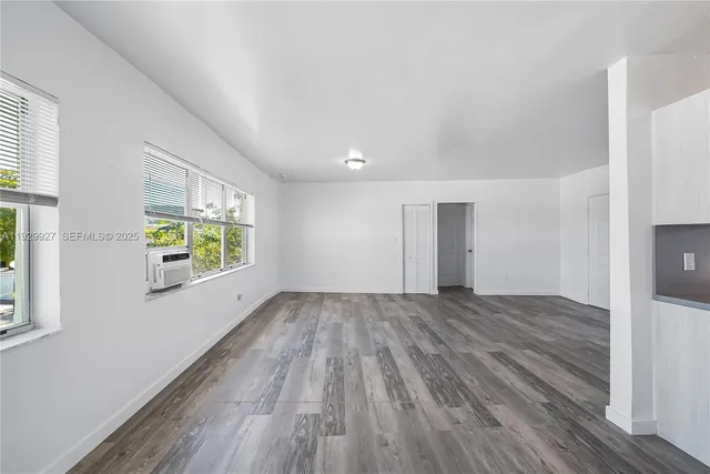 a view of empty room with wooden floor and kitchen