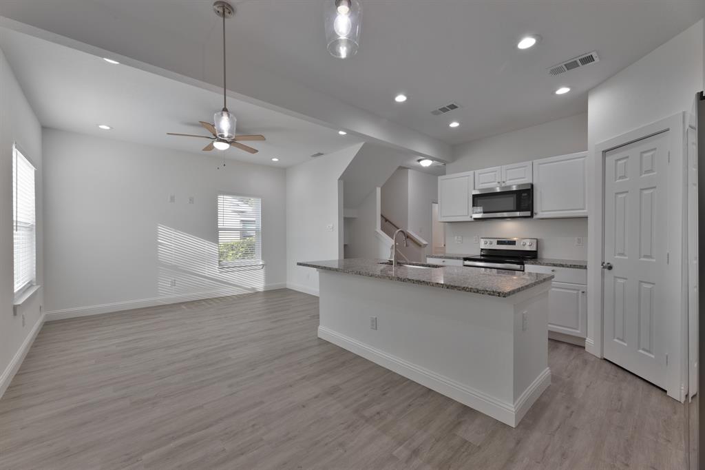 Kitchen featuring white cabinetry, light stone counters, a center island with sink, stainless steel appliances, and light wood-type flooring