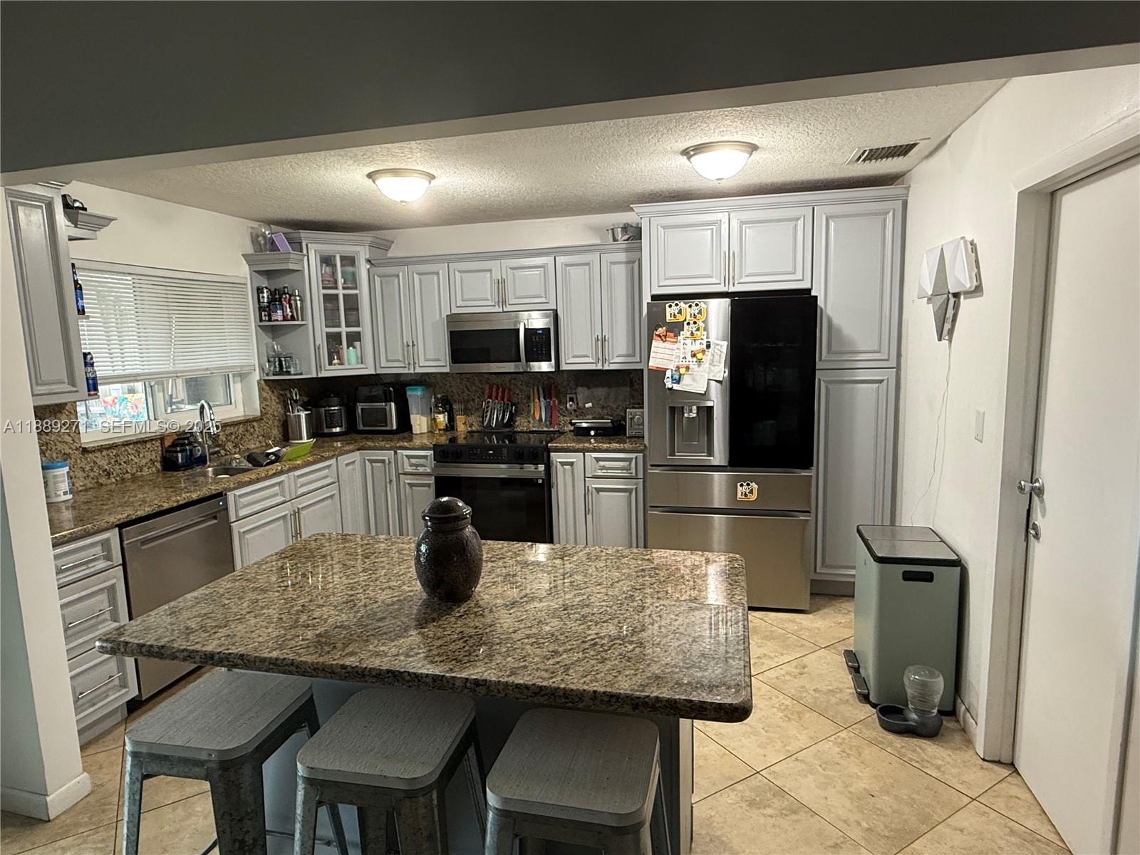 13060 Southwest 263rd Terrace Homestead, FL 33032 - Photo 8 of 30 a kitchen with kitchen island granite countertop a table chairs microwave and refrigerator
