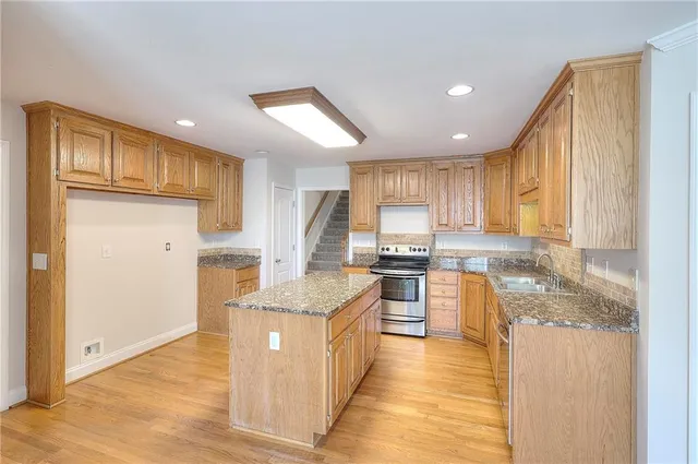 a kitchen with stainless steel appliances granite countertop a refrigerator a sink dishwasher a stove with wooden cabinets and floor