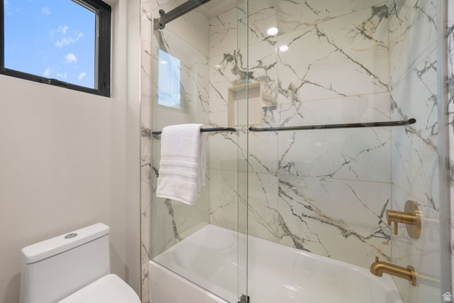 10646 North Reflection Ridge Hideout, UT 84036 - Photo 22 of 43 Bathroom featuring a tub and shower combination with glass enclosure, large format marble-look tile surround, a built-in shower niche, and brass fixtures