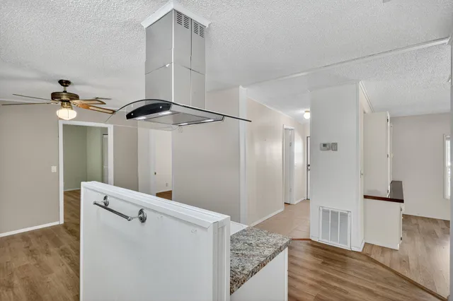 an empty room with wooden floor chandelier fan and windows