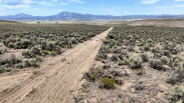 123 East Tbd 5000 Road North Panguitch, UT 84759 - Photo 35 of 54 Expansive desert landscape with a clear dirt road, low-lying brush, and distant mountains under a blue sky with scattered clouds