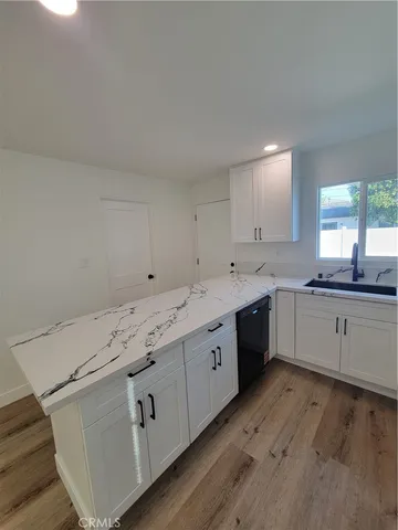 a large white kitchen with a sink dishwasher a stove and white cabinets with wooden floor