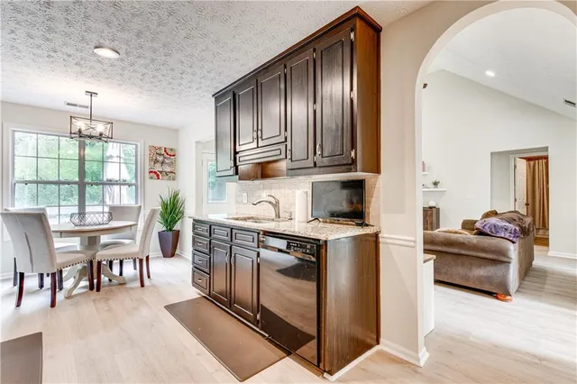 a kitchen with stainless steel appliances granite countertop a stove top oven a sink dishwasher a dining table and chairs with wooden floor