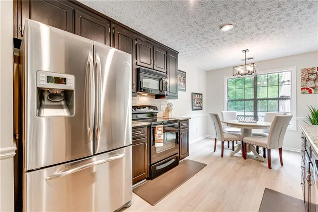 a kitchen with stainless steel appliances a refrigerator a stove a dining table and chairs with wooden floor