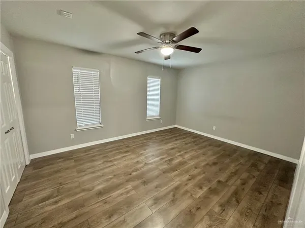an empty room with wooden floor fan and windows