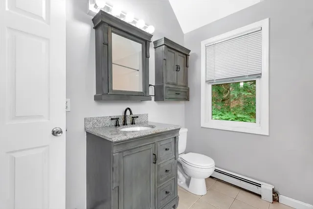a bathroom with a granite countertop toilet a sink a mirror and a window