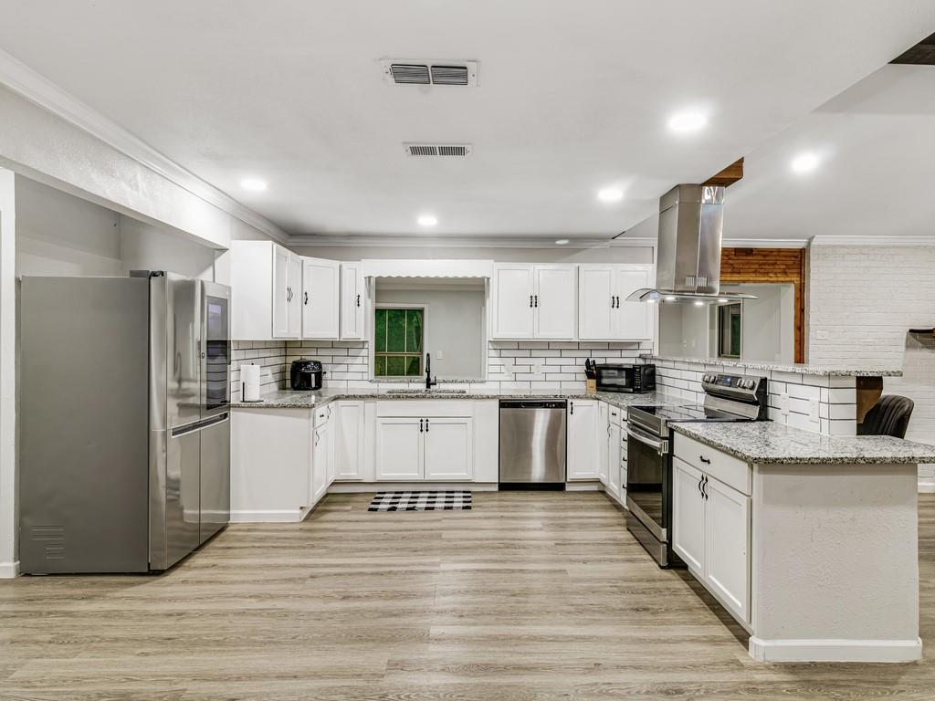 203 Hogg Street Streetman, TX 75859 - Photo 13 of 36 a kitchen with white cabinets stainless steel appliances and wooden floor