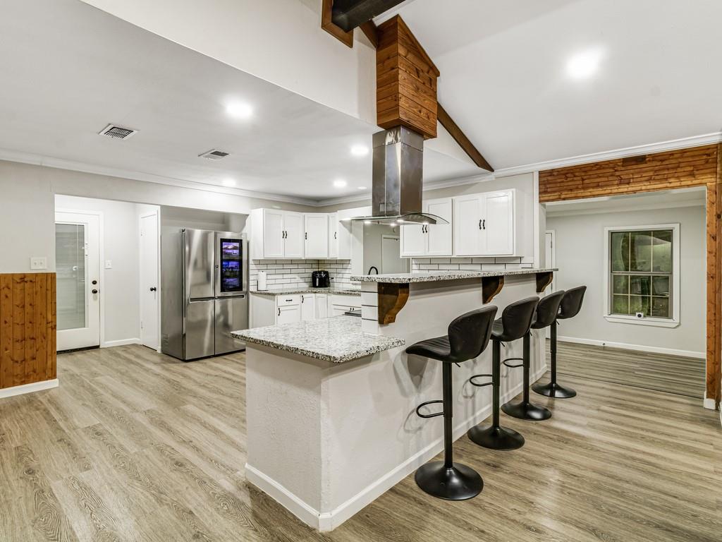 203 Hogg Street Streetman, TX 75859 - Photo 14 of 36 Kitchen with white cabinetry, ornamental molding, light stone counters, a kitchen breakfast bar, and light wood-type flooring