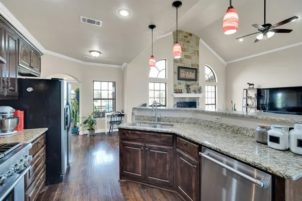 a kitchen with granite countertop a stove a sink dishwasher a dining table and chairs with wooden floor