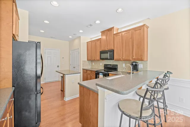 a kitchen with stainless steel appliances granite countertop a refrigerator a stove a sink a dining table and chairs with wooden floor