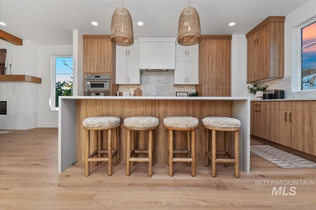 3219 West Moore Street Boise, ID 83702 - Photo 16 of 36 Kitchen island with white waterfall countertop, light wood-finish cabinetry, white upper cabinets, stainless steel built-in microwave, and pendant lighting